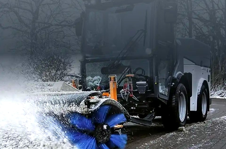 Kommunalfahrzeug mit Kehrwalze räumt Schnee von einem gepflasterten Weg