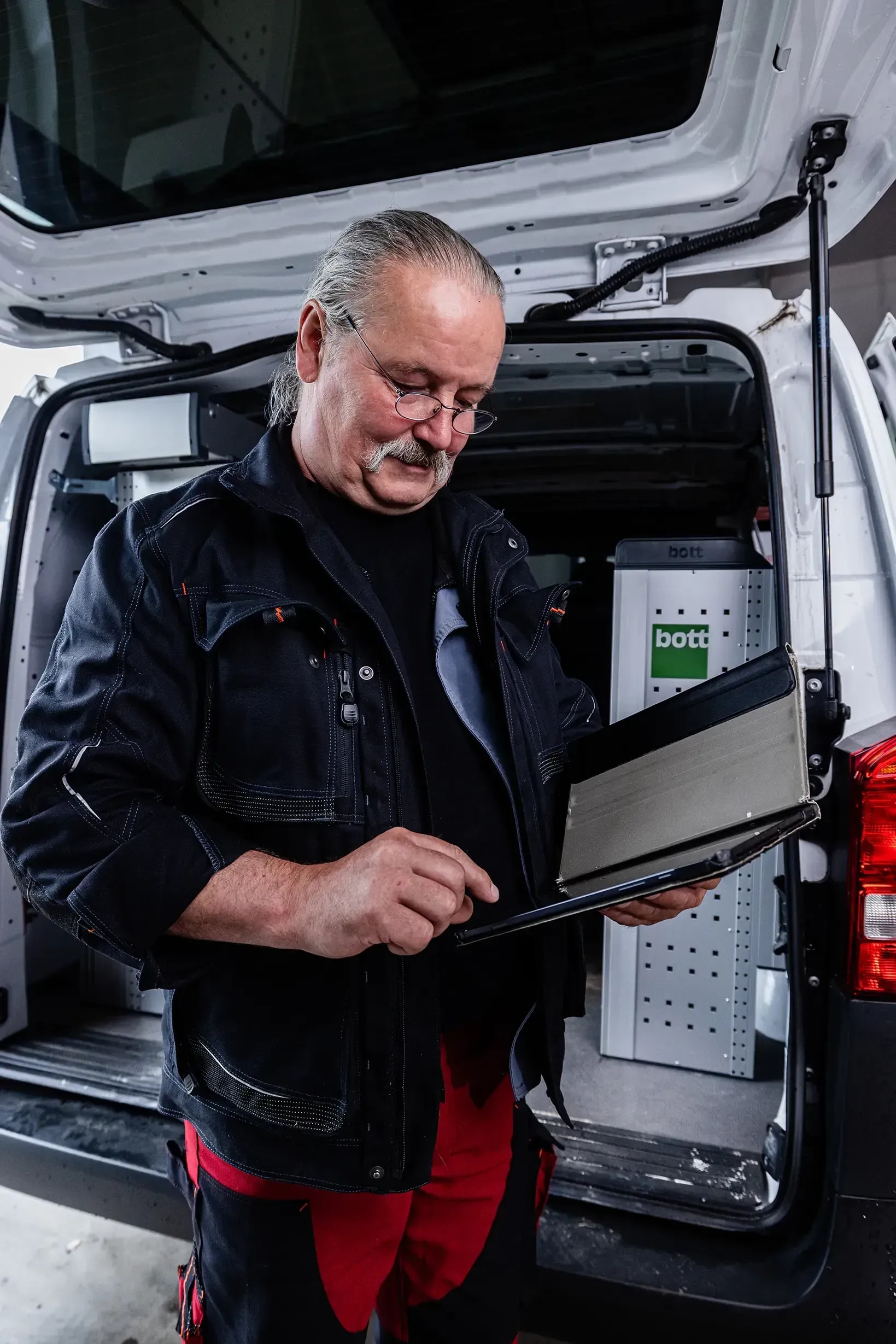 Servicetechniker mit Ordner am eingerichteten Werkstattwagen für Heizung und Kundendienst