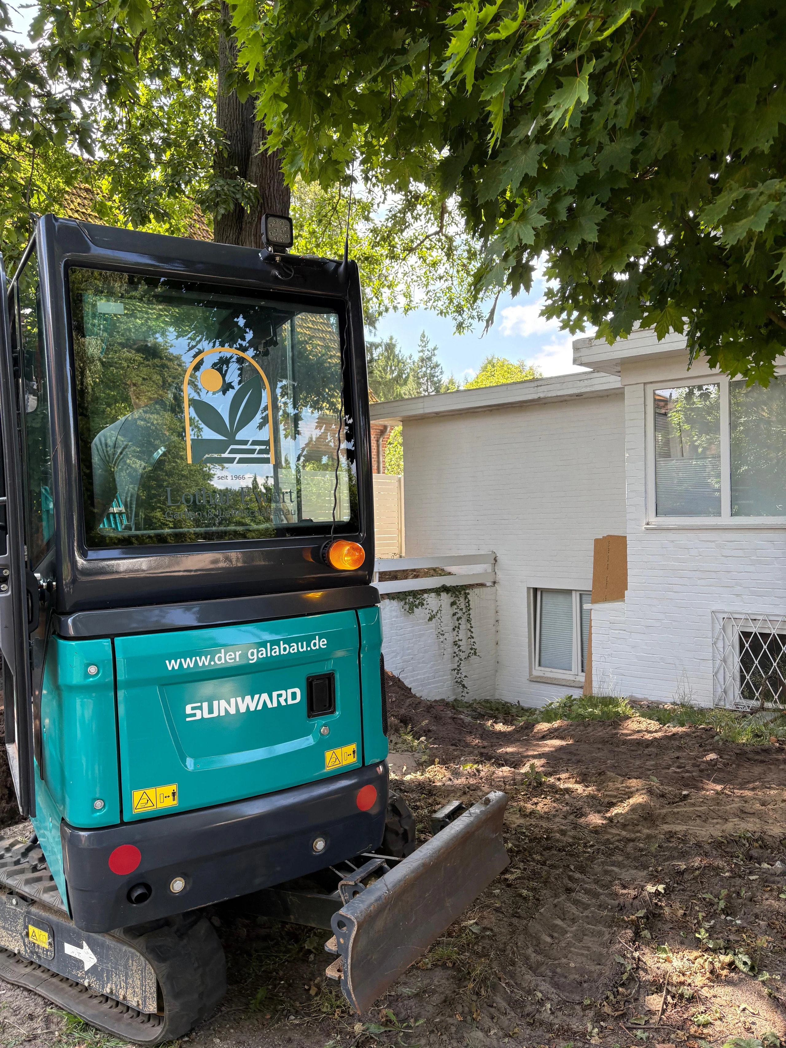 Minibagger Sunward mit Schaufel bei Erdarbeiten vor Wohnhaus im Garten- und Landschaftsbau