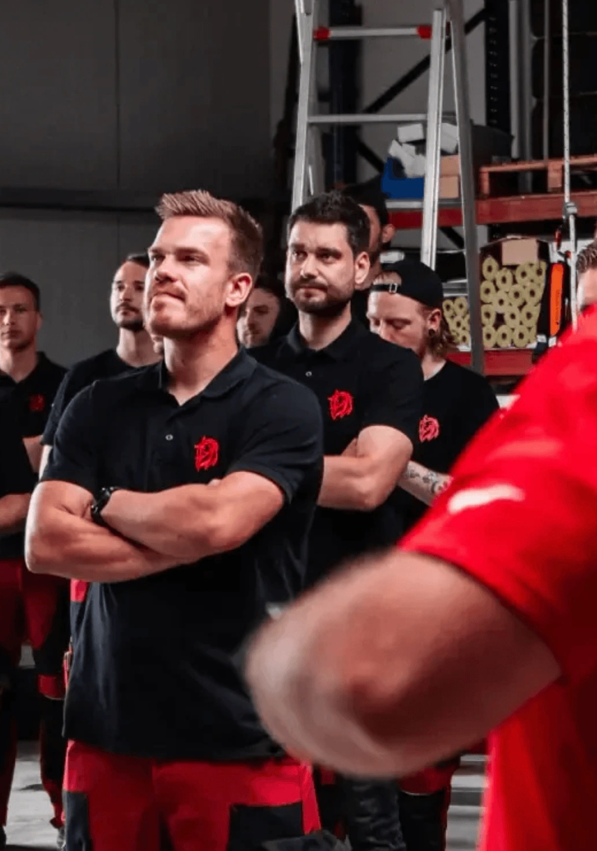 Team von Monteuren in schwarzen Poloshirts steht bei einer Schulung im Lager